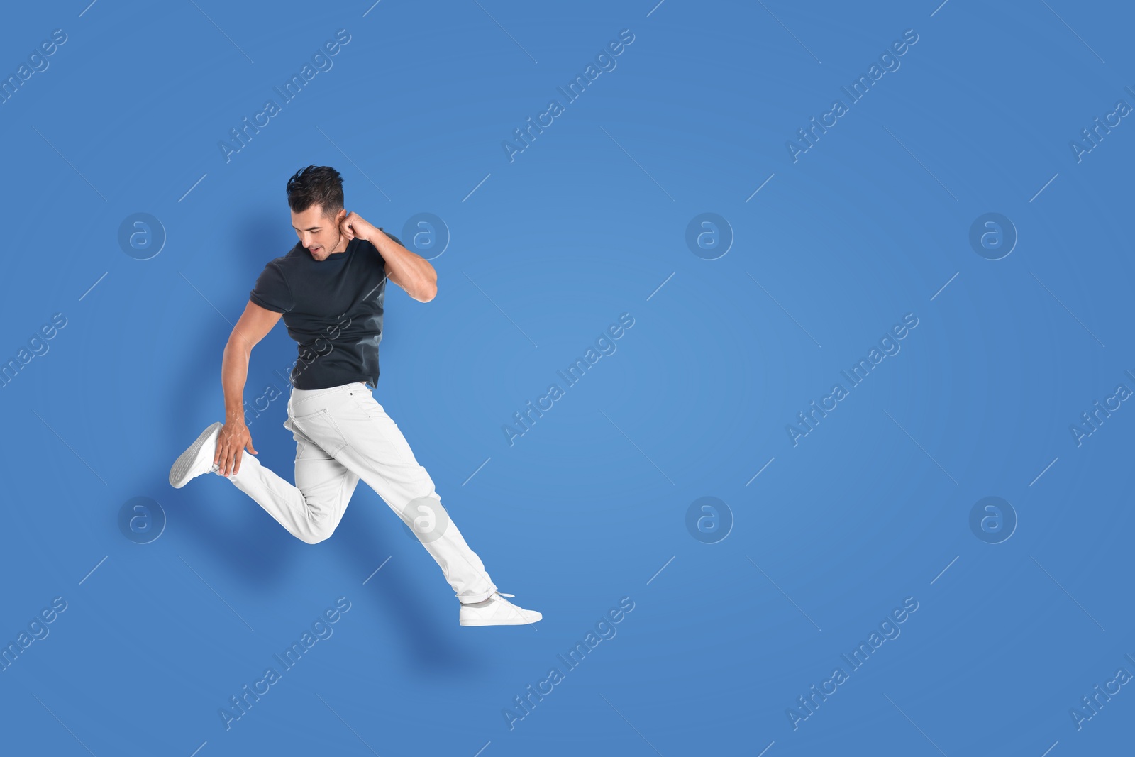 Image of Positive young man jumping on blue background. Space for text