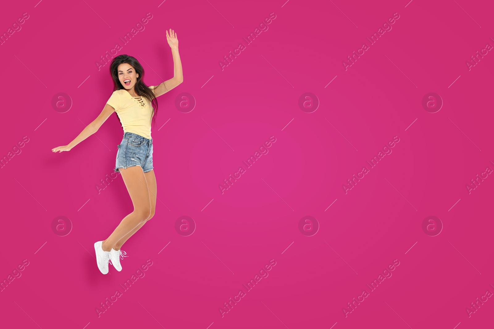 Image of Positive young woman jumping on hot pink background. Space for text