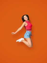 Image of Positive young woman jumping on dark orange background