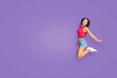 Positive young woman jumping on purple background. Space for text