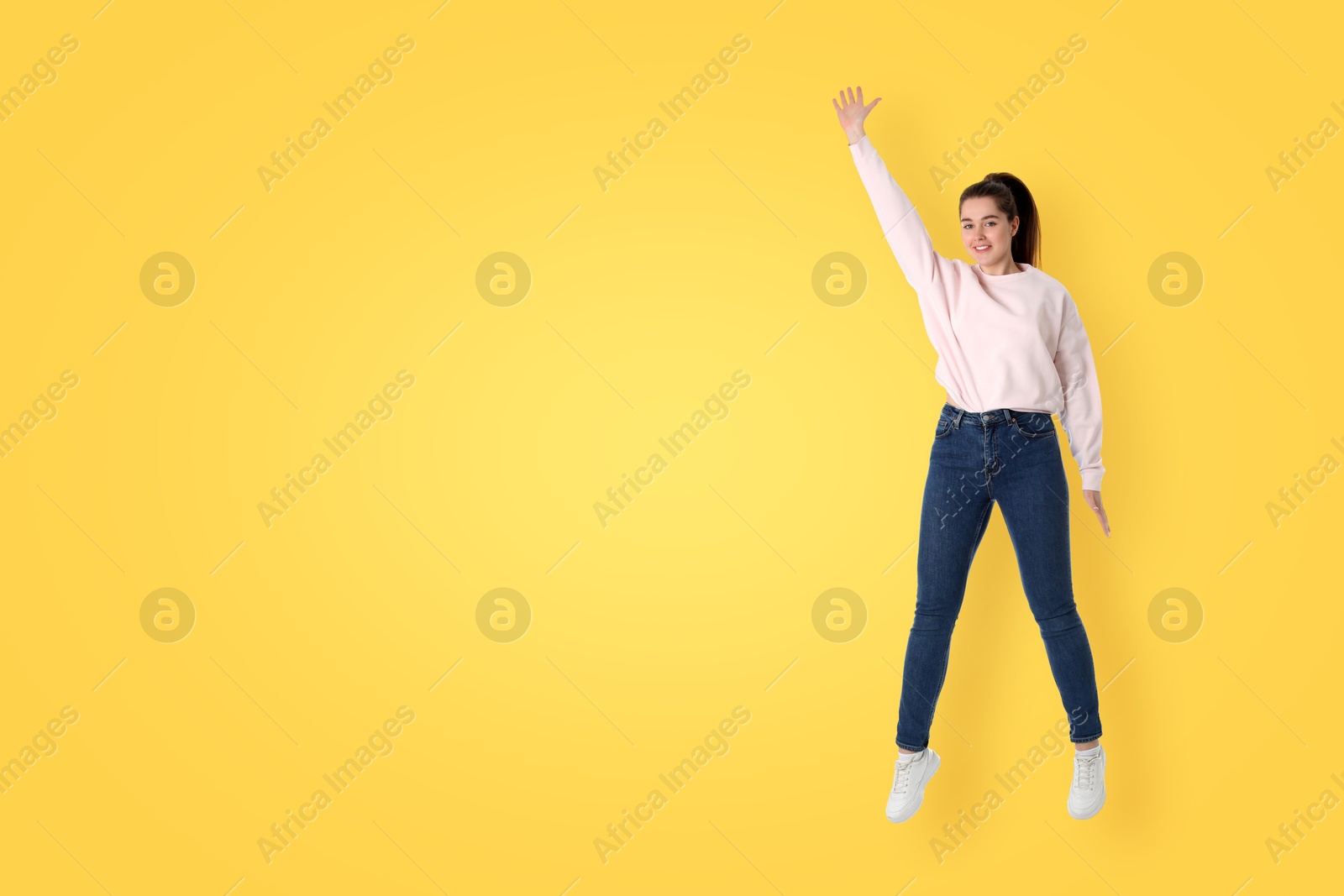 Image of Positive young woman jumping on yellow background. Space for text