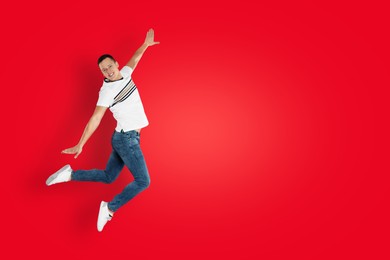 Positive young man jumping on red background. Space for text