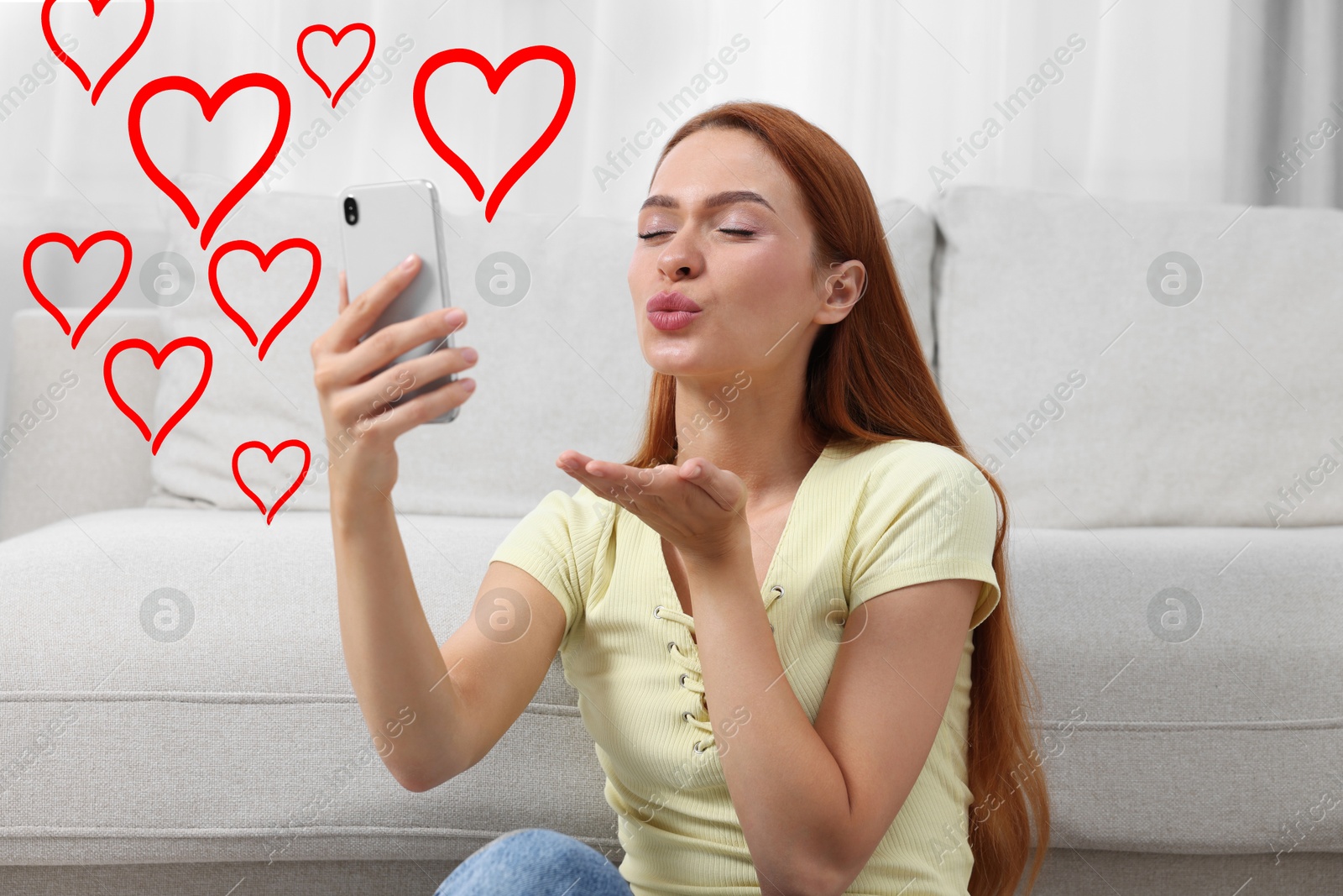 Image of Long distance relationship. Young woman sending air kiss to her loved one via video chat indoors. Red hearts near her