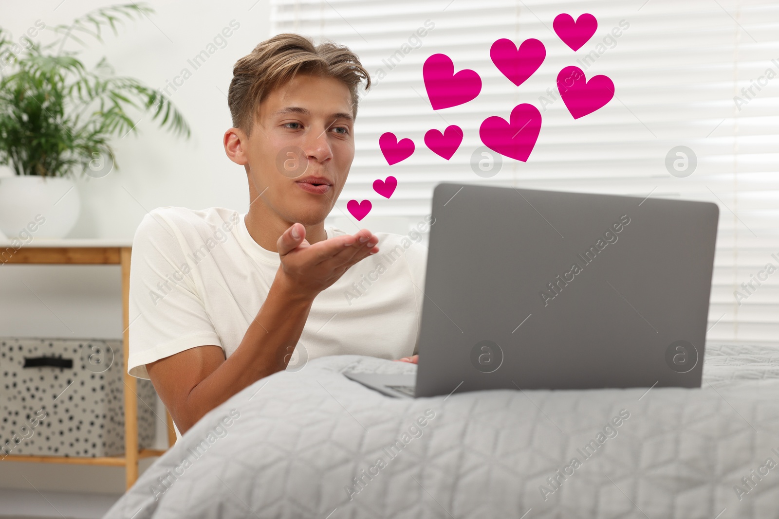 Image of Long distance relationship. Young man sending air kiss to his loved one via video chat indoors. Pink hearts near him