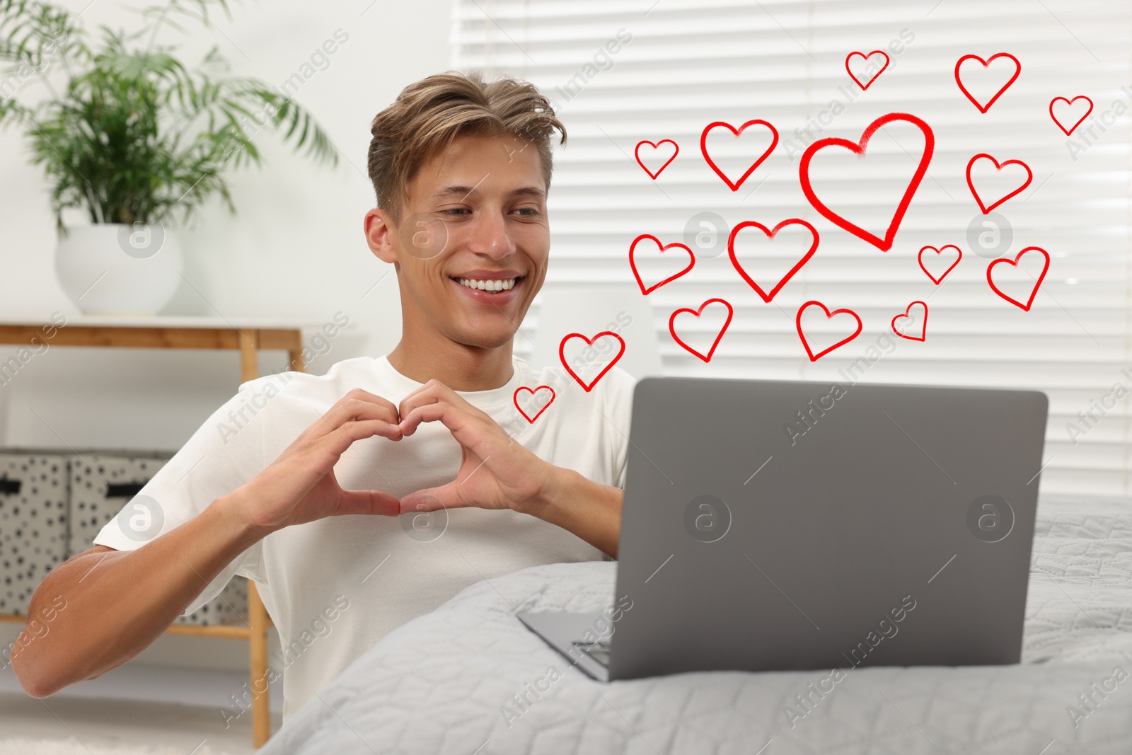 Image of Long distance relationship. Young man having video chat with his loved one indoors. Red hearts near him