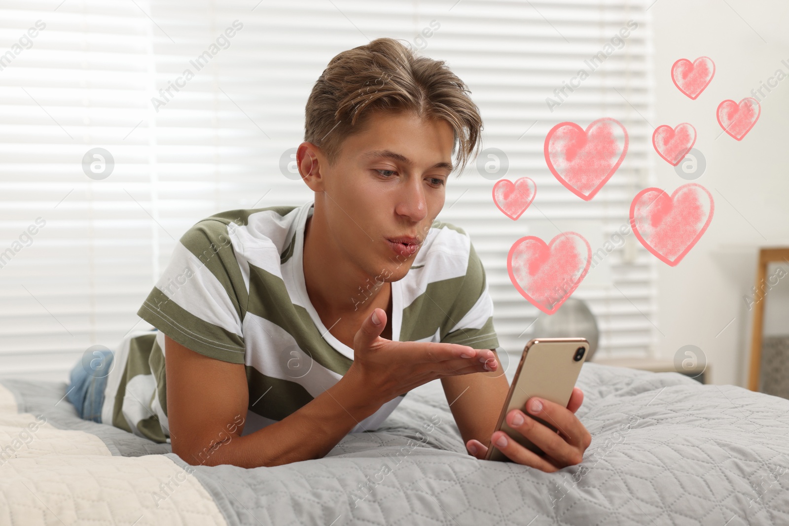 Image of Long distance relationship. Young man sending air kiss to his loved one via video chat indoors. Pink hearts near him