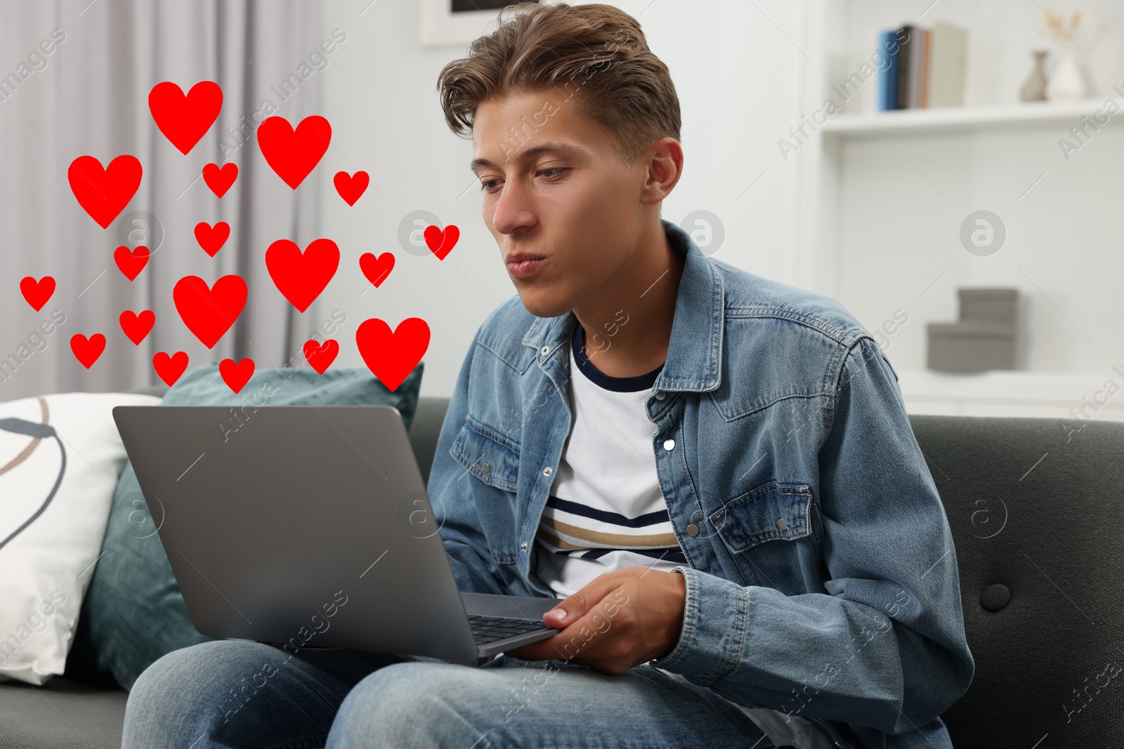 Image of Long distance relationship. Young man sending air kiss to his loved one via video chat indoors. Red hearts near him