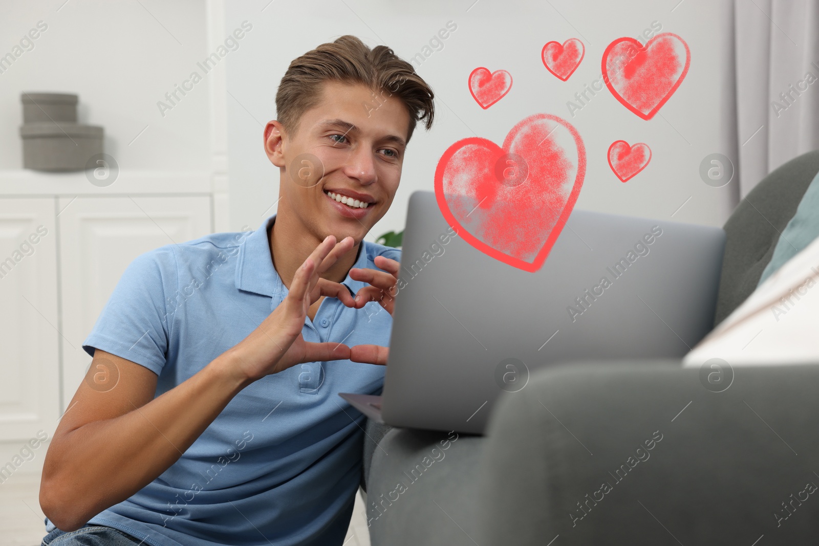 Image of Long distance relationship. Young man having video chat with his loved one indoors. Red hearts near him