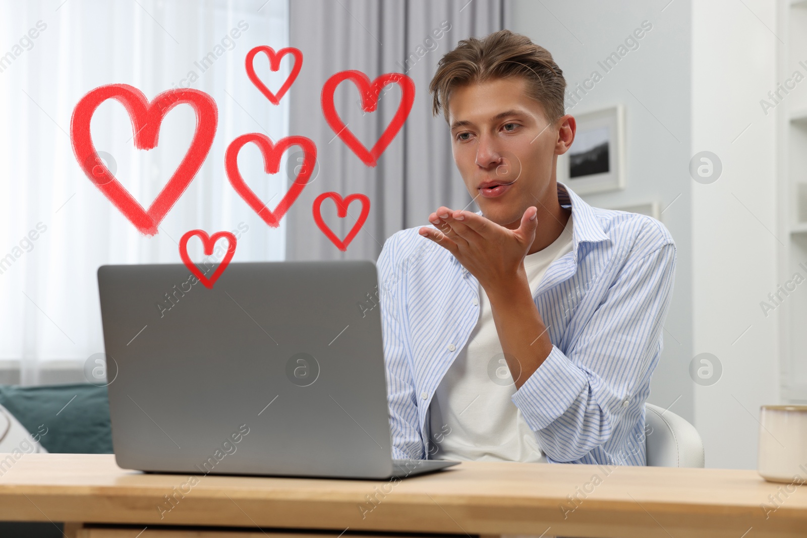 Image of Long distance relationship. Young man sending air kiss to his loved one via video chat indoors. Red hearts near him