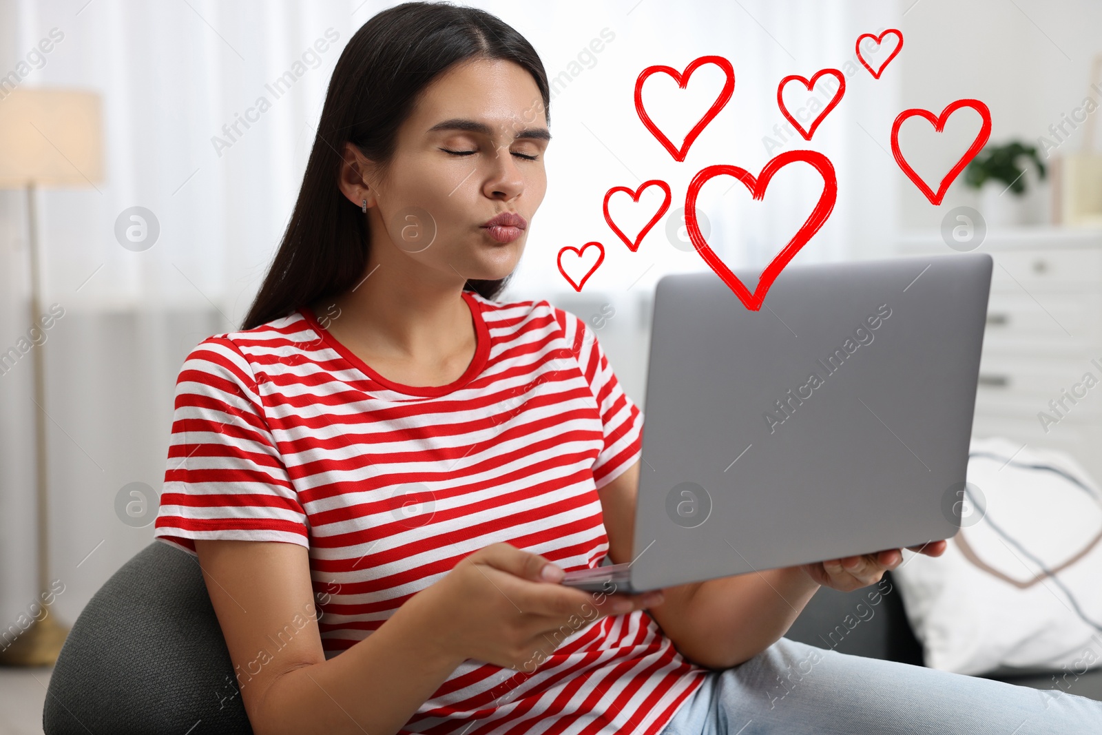 Image of Long distance relationship. Young woman sending air kiss to her loved one via video chat indoors. Red hearts near her