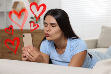 Long distance relationship. Young woman sending air kiss to her loved one via video chat indoors. Red hearts near her