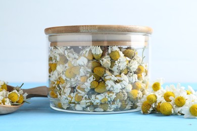 Photo of Dry and fresh chamomile flowers on light blue wooden table