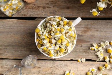 Photo of Chamomile flowers in cup and sieve on wooden table, flat lay