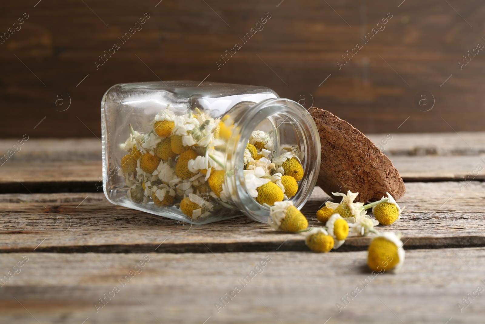 Photo of Chamomile flowers in glass jar on wooden table, closeup