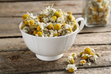 Photo of Chamomile flowers in cup on wooden table, closeup