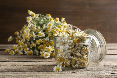 Photo of Dry and fresh chamomile flowers in glass jar on wooden table