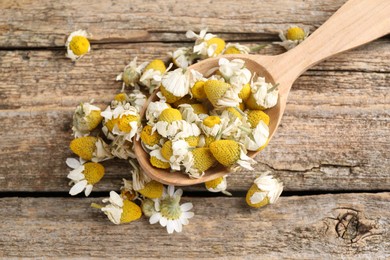 Photo of Chamomile flowers in spoon on wooden table, top view