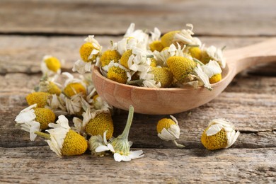 Photo of Chamomile flowers and spoon on wooden table, closeup