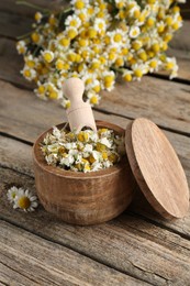 Photo of Dry and fresh chamomile flowers with scoop in bowl on wooden table