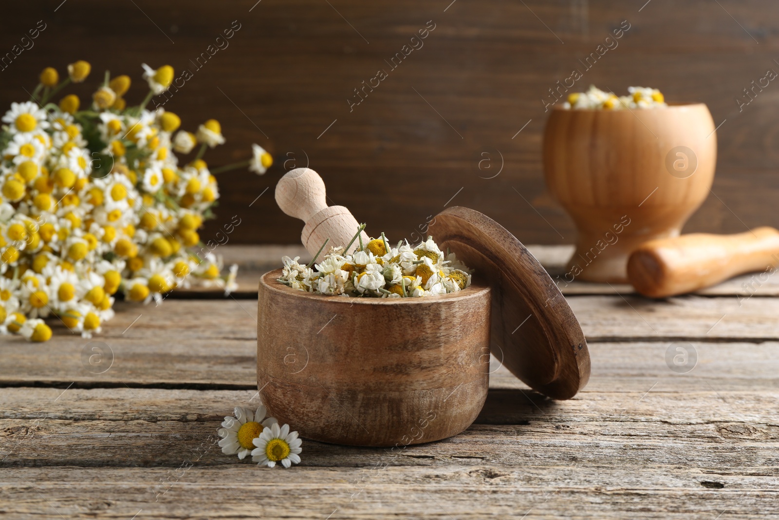 Photo of Dry and fresh chamomile flowers with scoop in bowl on wooden table