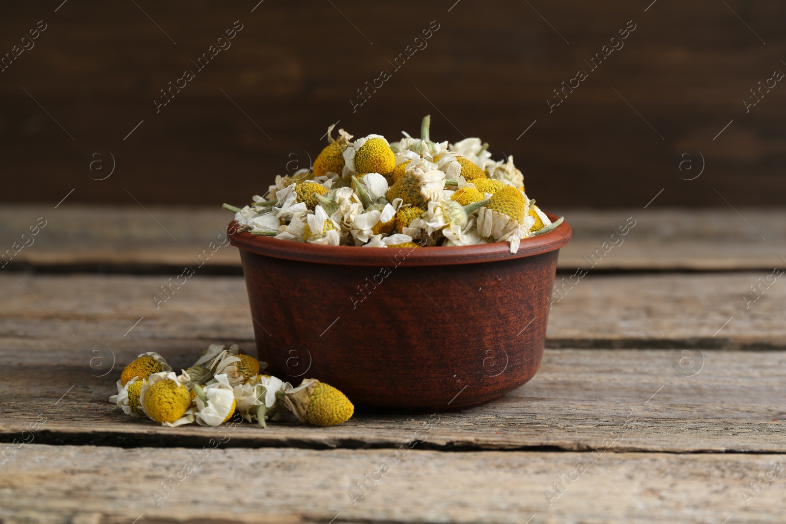 Photo of Chamomile flowers in bowl on wooden table, closeup