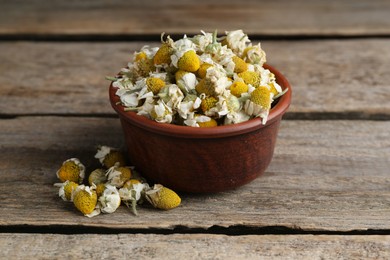 Photo of Chamomile flowers in bowl on wooden table, closeup