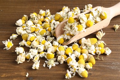 Photo of Chamomile flowers and scoop on wooden table