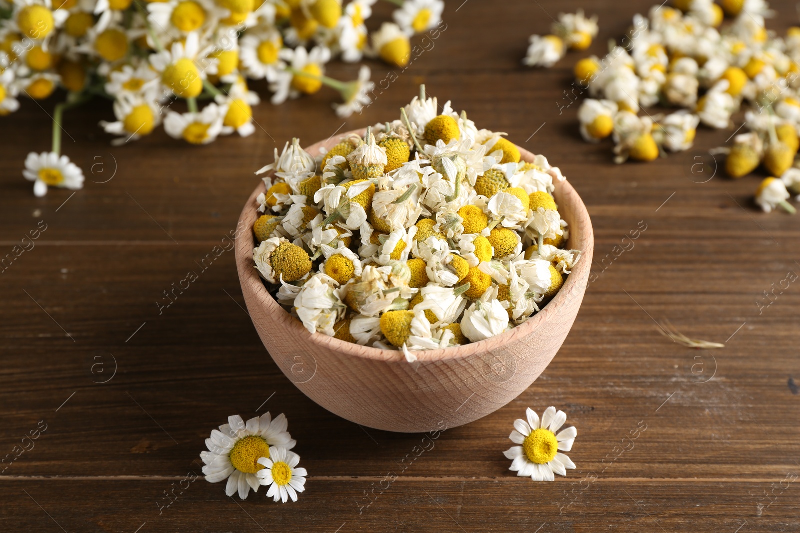 Photo of Dry and fresh chamomile flowers in bowl on wooden table