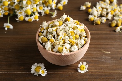 Dry and fresh chamomile flowers in bowl on wooden table