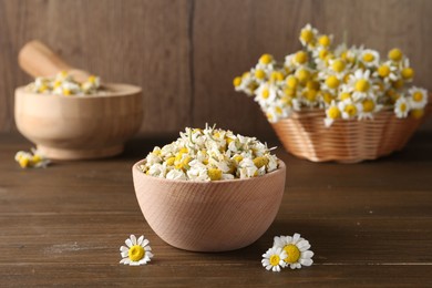 Photo of Dry and fresh chamomile flowers in bowl on wooden table