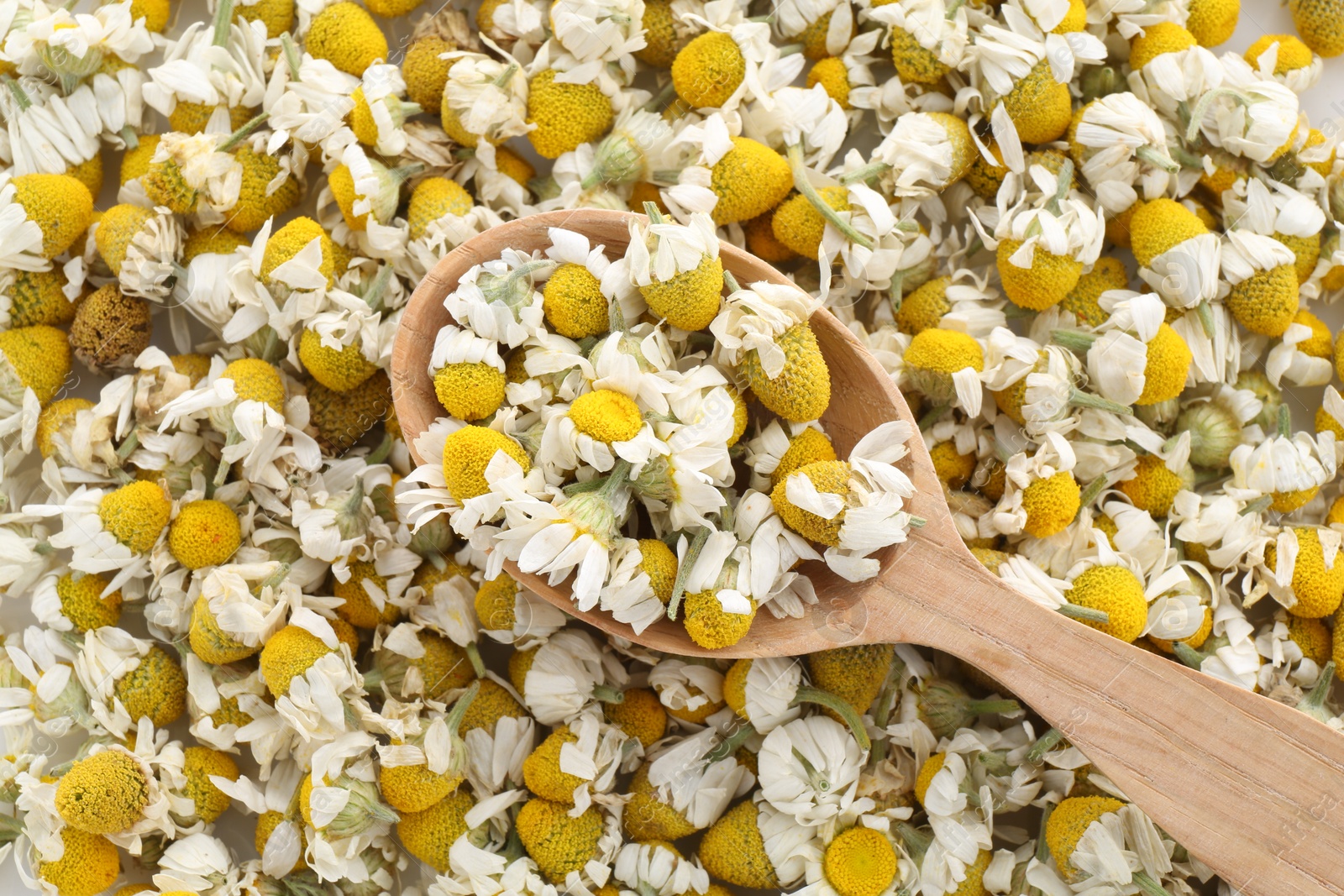 Photo of Wooden spoon on chamomile flowers, top view