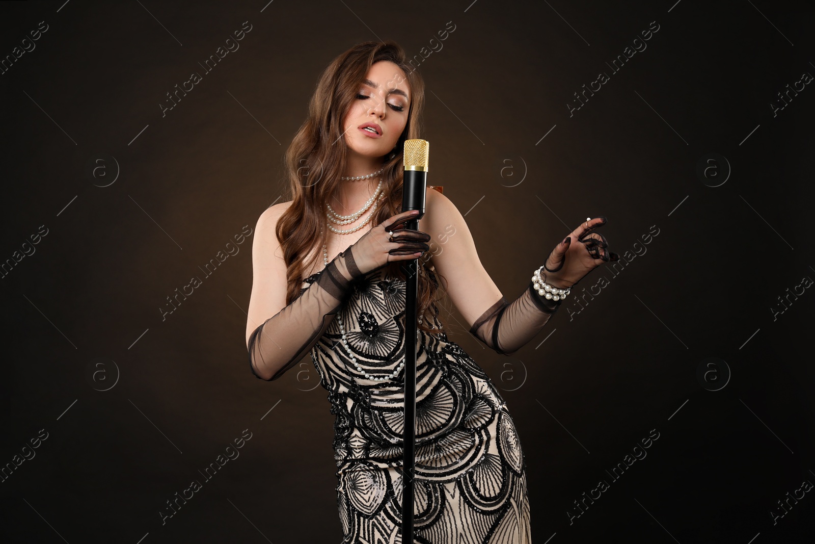 Photo of Beautiful young woman in stylish dress with microphone singing on dark background