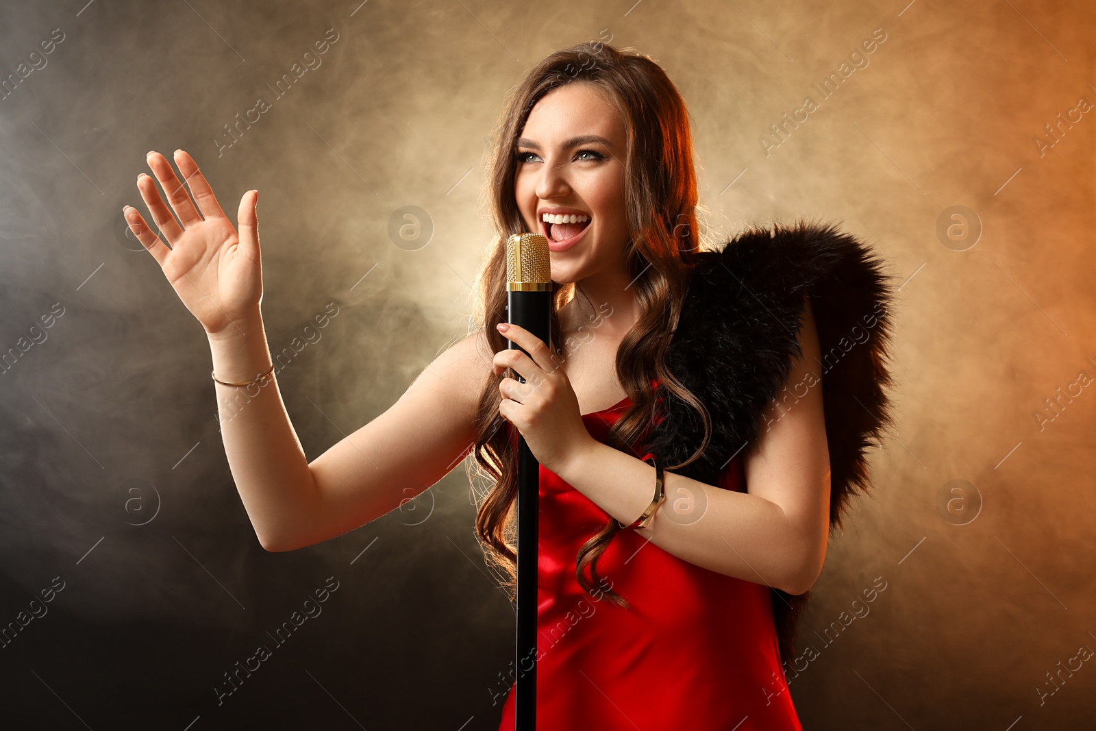 Photo of Beautiful young woman in stylish dress with microphone singing on dark background in color lights and smoke