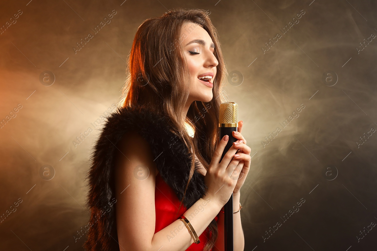 Photo of Beautiful young woman with microphone singing on color background with smoke