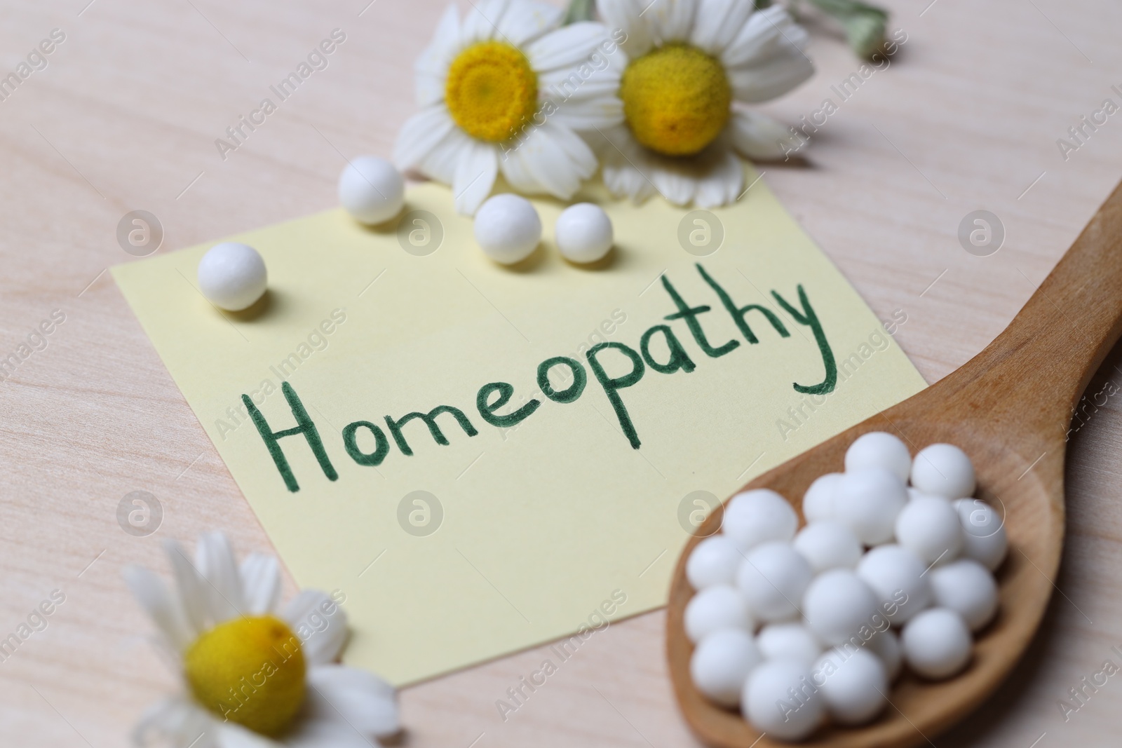 Photo of Sticky note with word Homeopathy, pills and chamomile flowers on wooden table, closeup