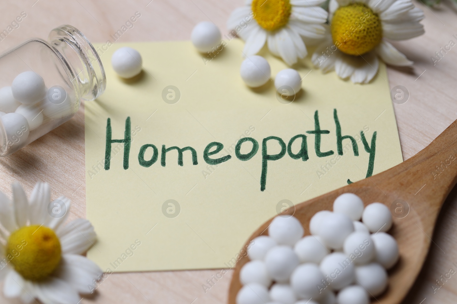 Photo of Sticky note with word Homeopathy, pills and chamomile flowers on wooden table, closeup