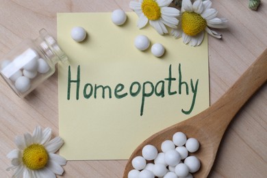 Photo of Sticky note with word Homeopathy, pills and chamomile flowers on wooden table, flat lay