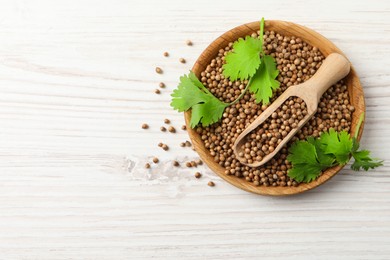 Photo of Dried coriander seeds with green leaves in bowl and scoop on wooden table, top view. Space for text