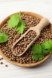 Photo of Dried coriander seeds with green leaves in bowl and scoop on wooden table, top view