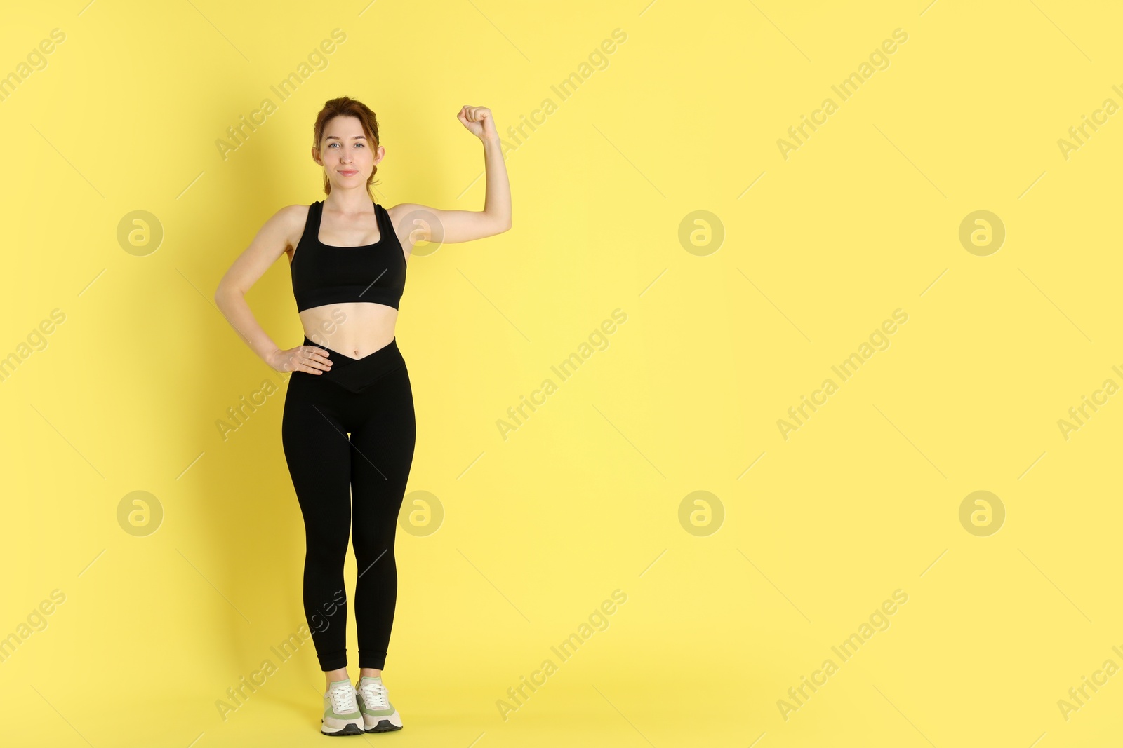 Photo of Woman with slim body showing muscles on yellow background, space for text