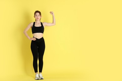 Woman with slim body showing muscles on yellow background, space for text