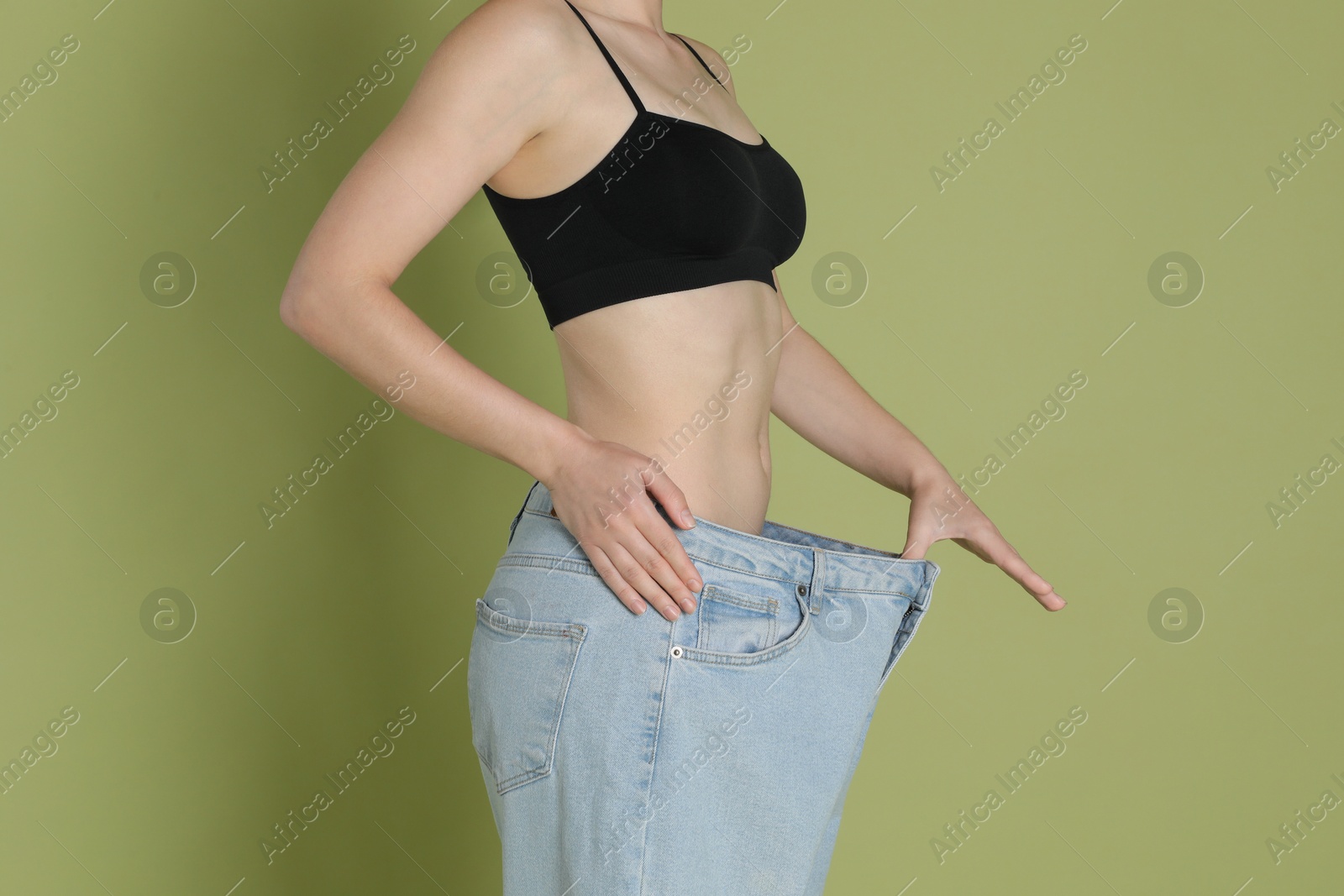 Photo of Woman in big jeans showing her slim body on olive background, closeup