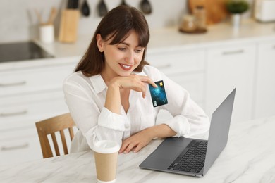 Photo of Online banking. Smiling woman with credit card and laptop paying purchase at table indoors