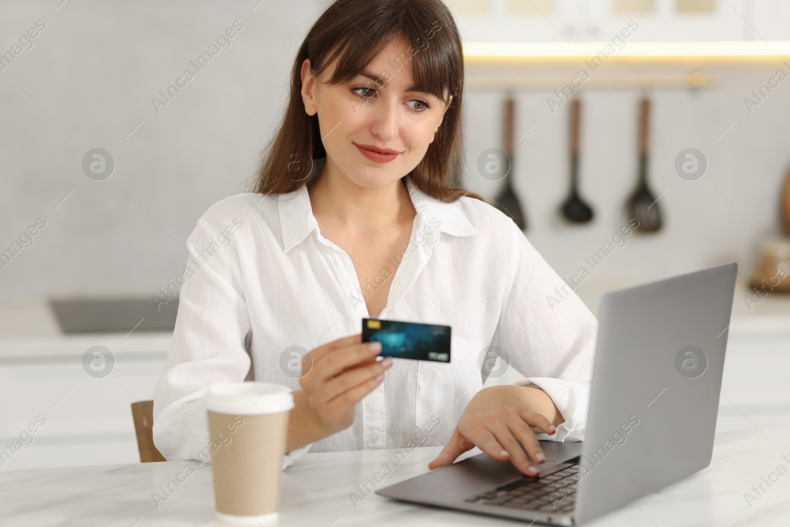 Photo of Online banking. Woman with credit card and laptop paying purchase at table indoors