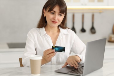 Online banking. Woman with credit card and laptop paying purchase at table indoors