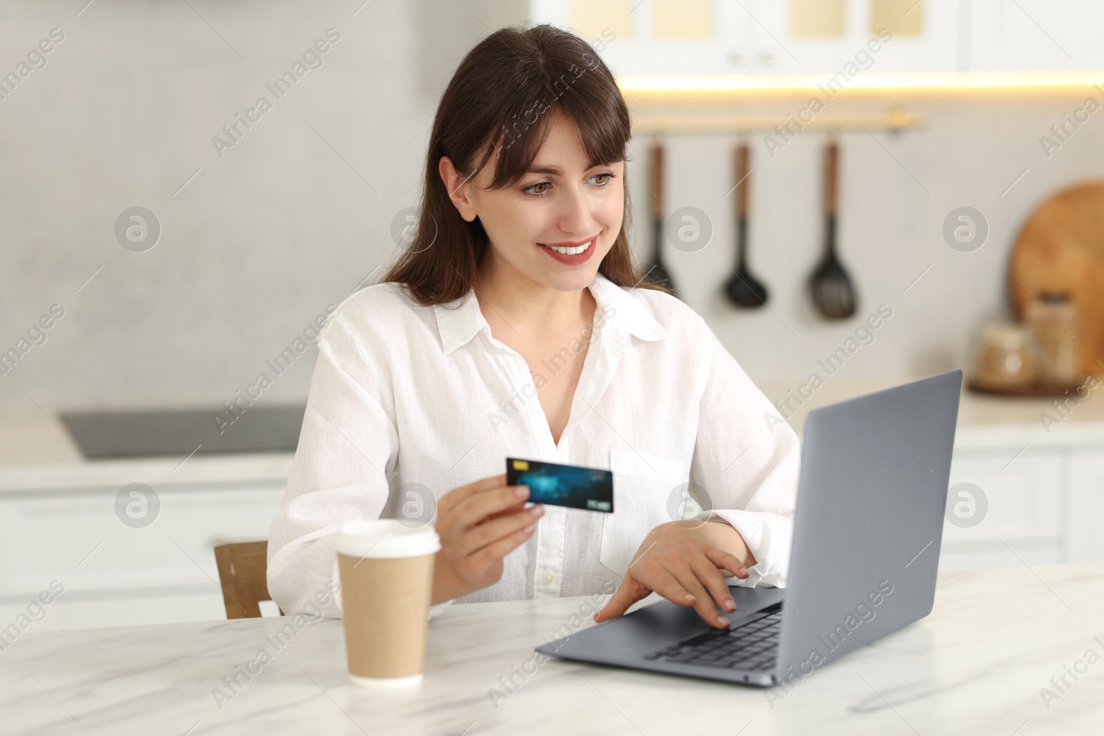 Photo of Online banking. Smiling woman with credit card and laptop paying purchase at table indoors