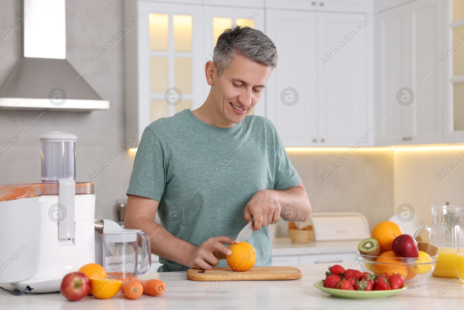 Photo of Juicer and fresh products on white marble table. Smiling man cutting orange in kitchen