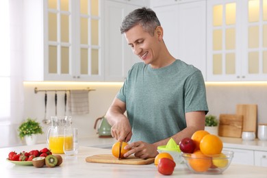Photo of Making juice. Smiling man cutting fresh orange at white marble table in kitchen