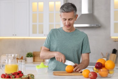 Photo of Making juice. Man cutting fresh orange at white marble table in kitchen