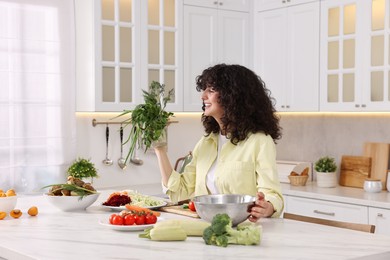 Photo of Woman cooking healthy vegetarian meal at white marble table in kitchen
